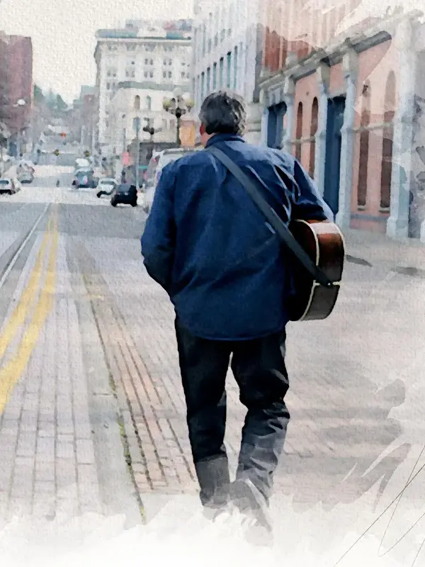 Mark seen from behind, walking down a road lined with brick buildings