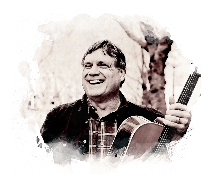 Mark smiling big, holding a guitar, trees in the distance