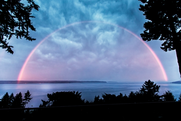 A full pink rainbow spanning over the water.